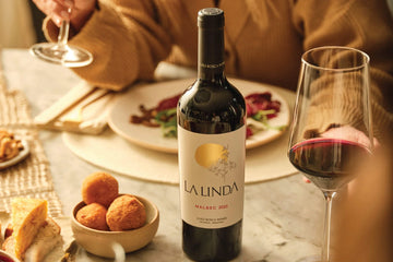 Bottle of La Linda Malbec wine with a glass of wine and snacks on a table.