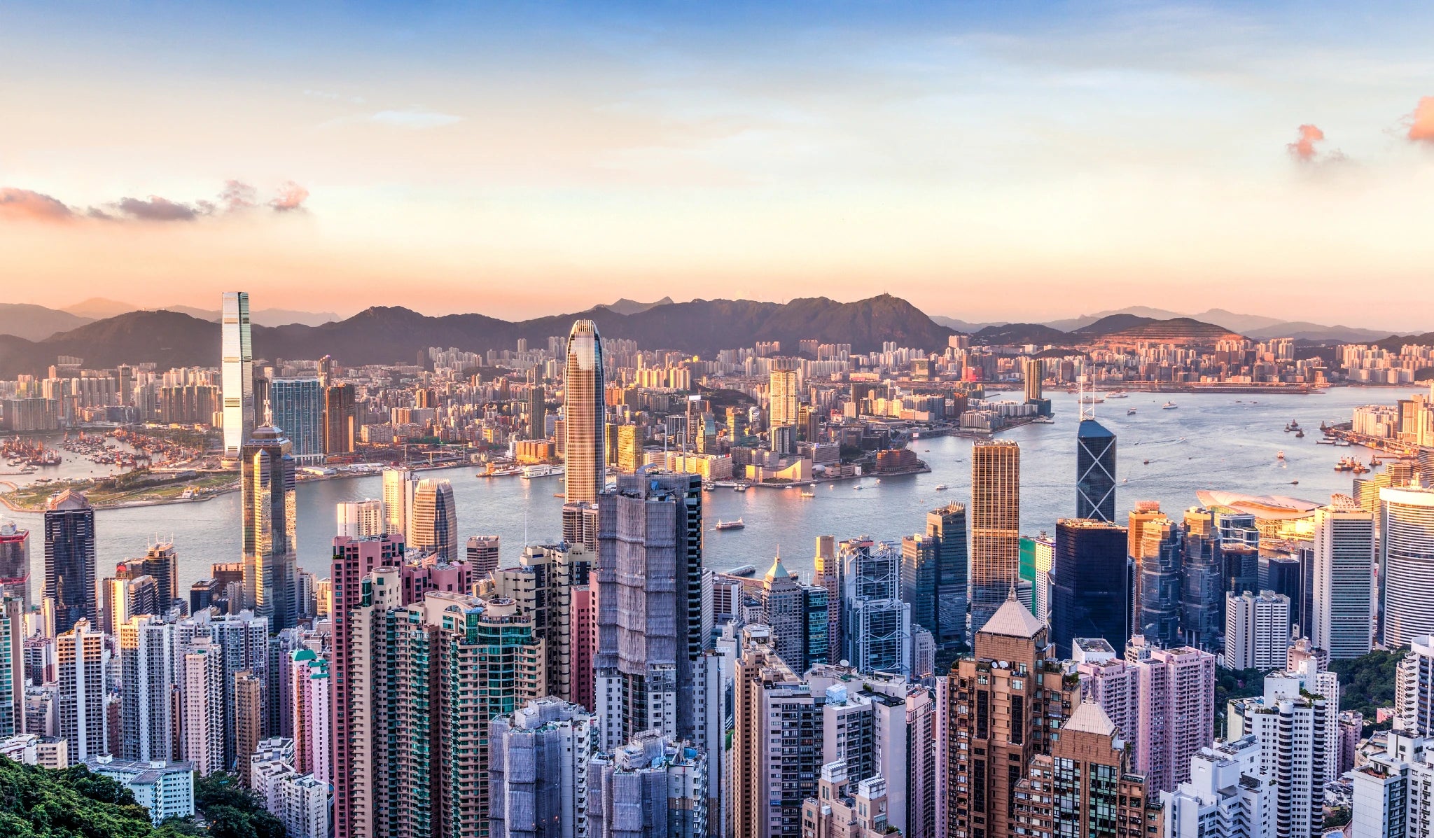 Hong Kong skyline with modern skyscrapers and a harbor at sunset.