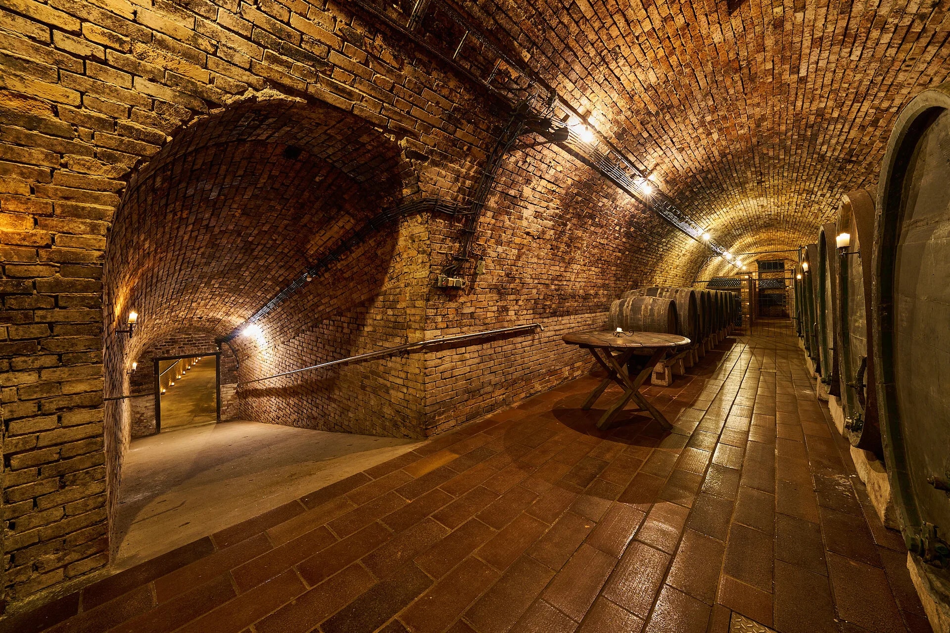 An arched brick cellar corridor lined with oak barrels