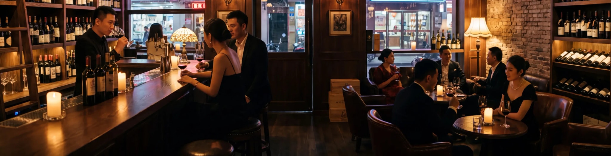 A candlelit wine bar in the evening: a bartender pours behind the counter while guests talk over glasses of red wine at the tables.