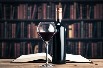 A bottle of red wine and a glass placed beside a historical book.
