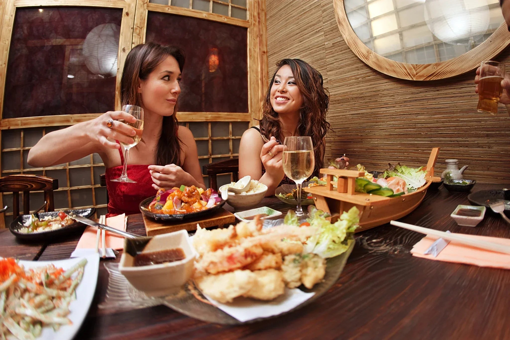 Two women enjoying spicy Asian food and appreciating glasses of white wine.