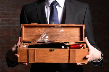 A man in a suit holding a wooden wine gift box with a bottle of red wine inside.