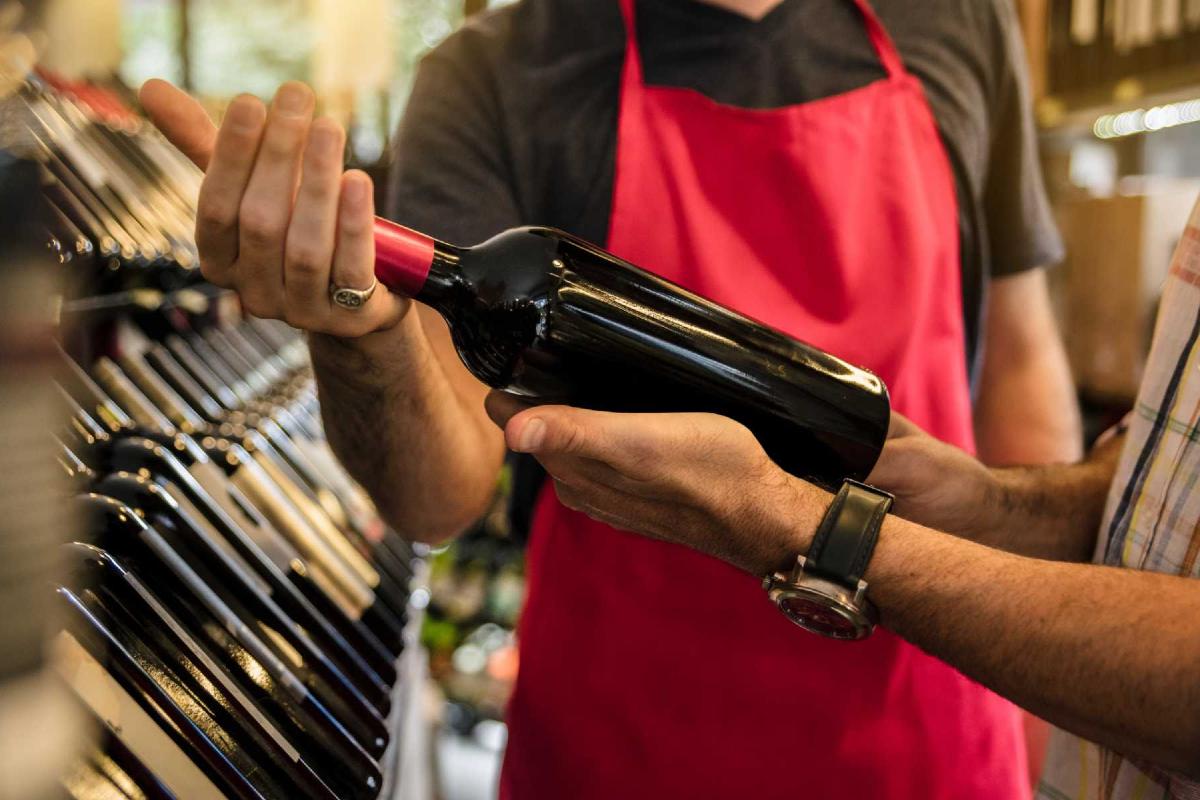 Customer examining a bottle of red wine with guidance from a wine shop salesperson.